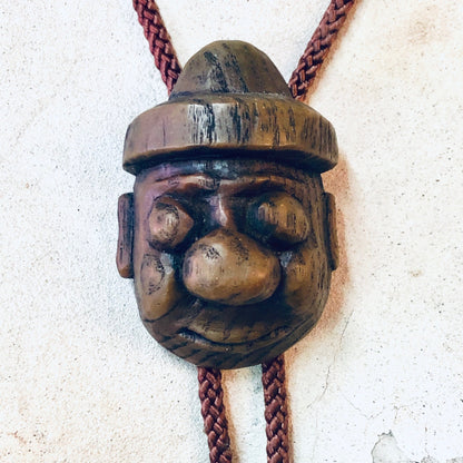 Vintage Japanese wooden carved face bolo tie with braided rope on textured background.