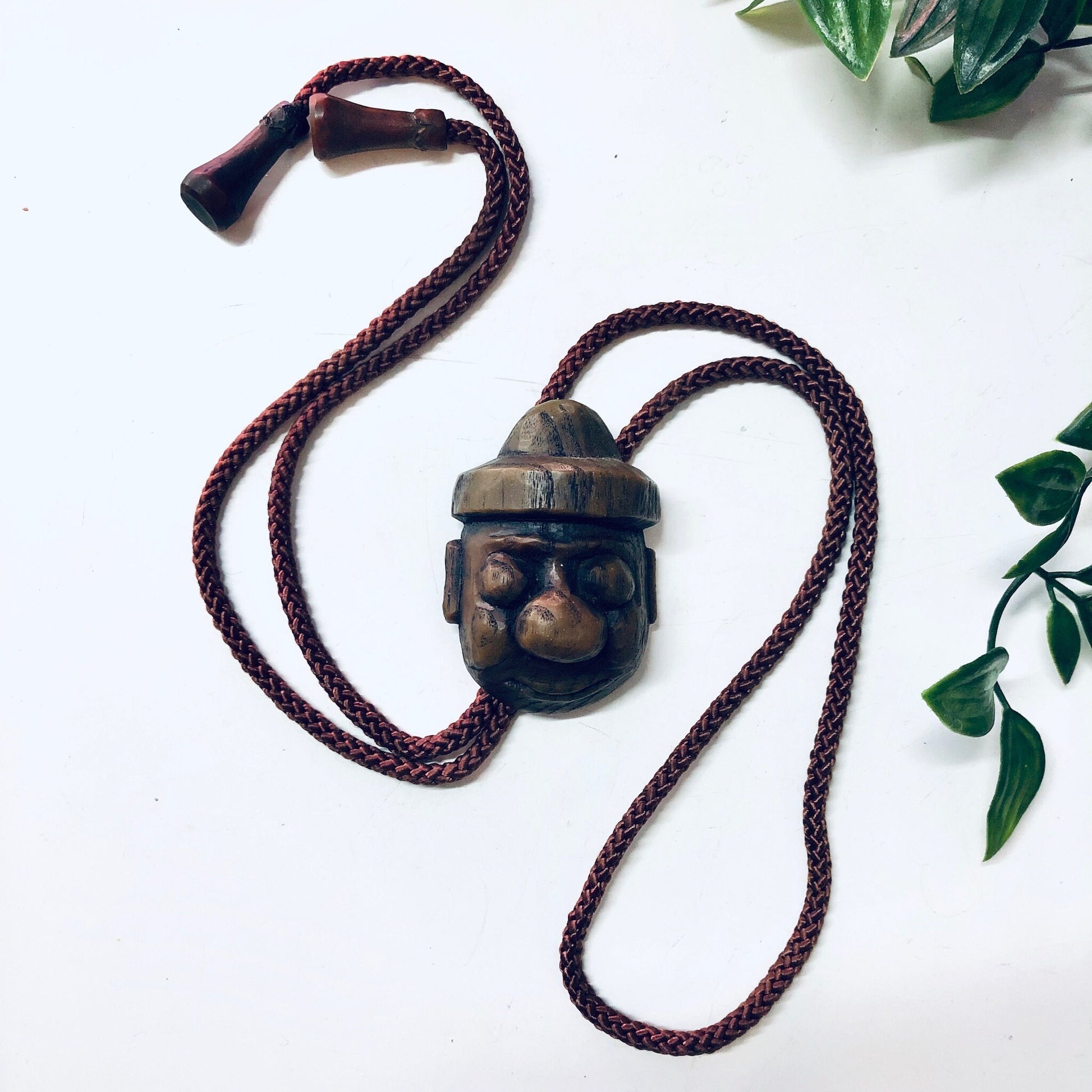 Vintage Japanese bolo tie with carved wooden face pendant and brown braided rope cord, unique retro accessory.