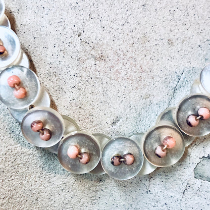 Vintage button necklace with pearlescent white and pink beads on textured grey background