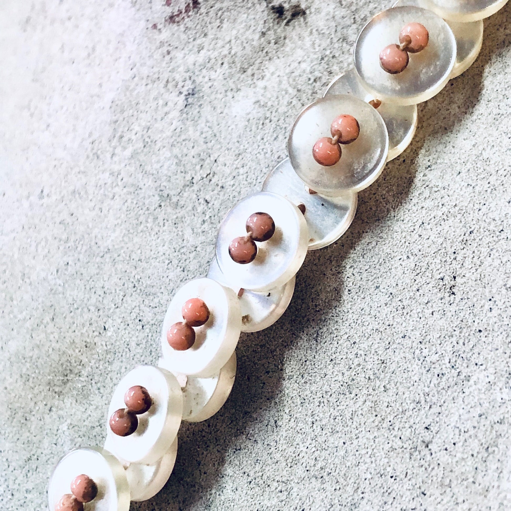 White pearlescent vintage button necklace with pink beads on stone surface