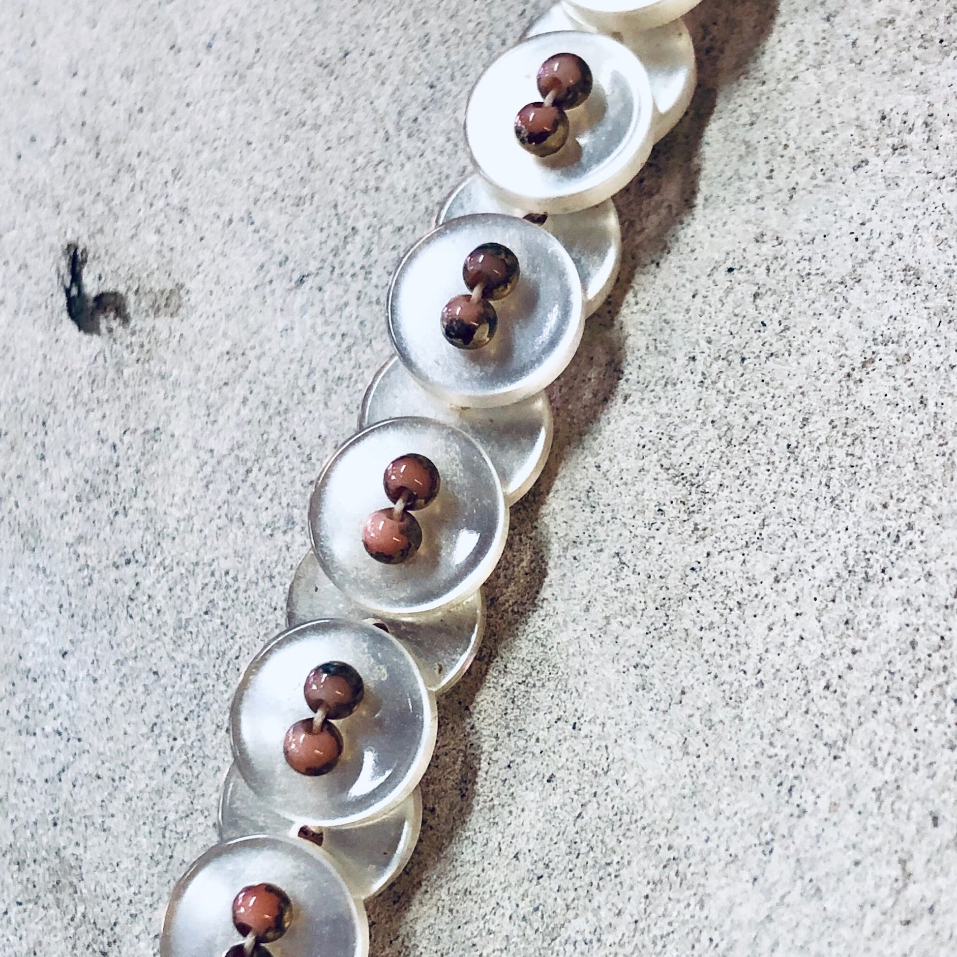 Vintage white pearlescent button necklace with pink beads on gray textured background