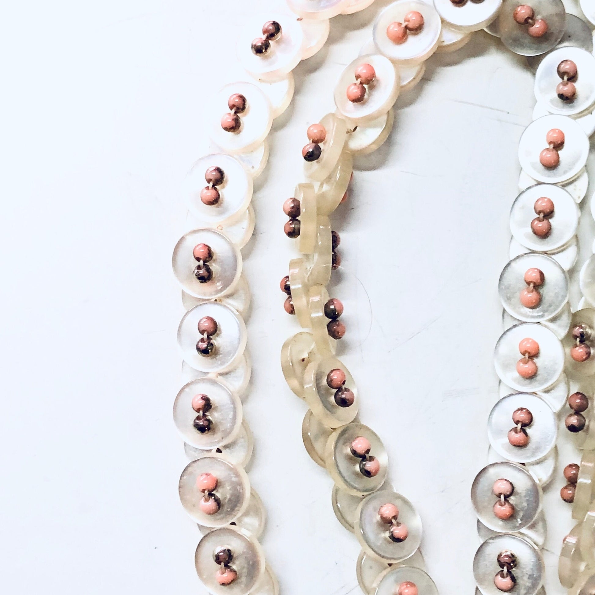 Vintage white button necklace with pearlescent pink beads strung together in multiple strands, creating a unique and elegant piece of button jewelry.