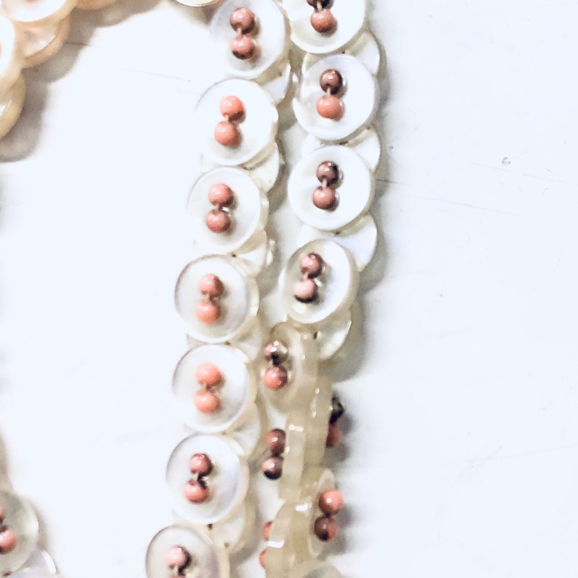 Vintage white pearlescent button necklace with pink beads on strand, close-up view of button jewelry and beaded necklace details