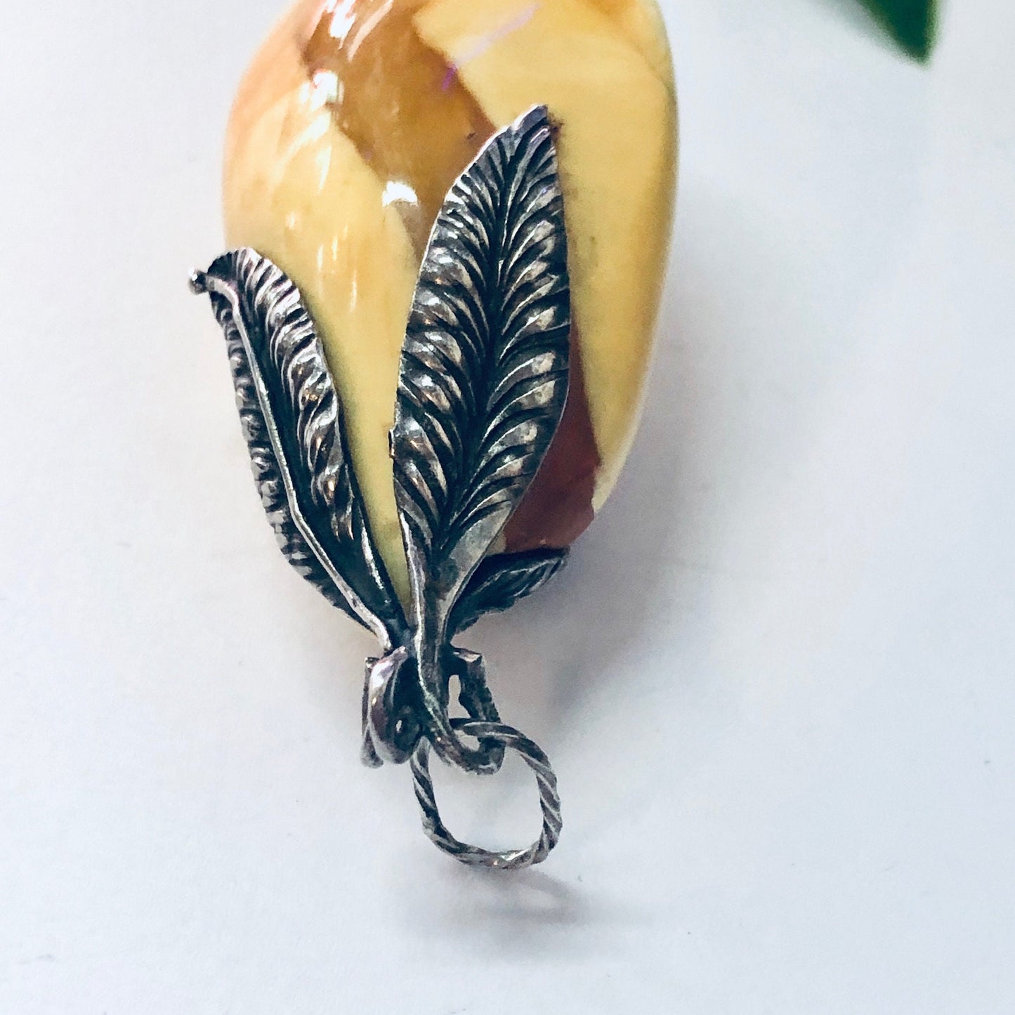 Silver pendant with butterscotch amber stone and ornate milky white silver feather or leaf design attached to the bottom of the amber stone.