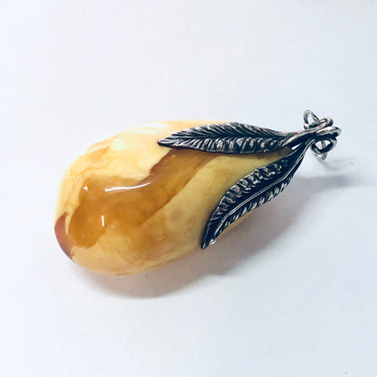 Vintage silver pendant featuring a large butterscotch amber stone with yellow and milky hues, crafted into a delicate feather shape.