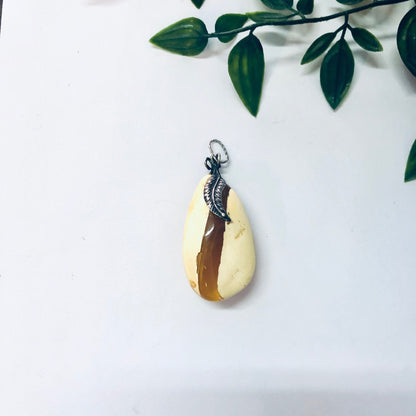 Vintage butterscotch amber pendant necklace with milky yellow amber set in silver, shown hanging from leafy branch.