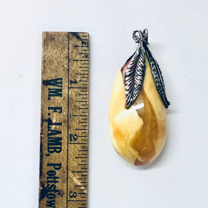 Vintage butterscotch amber pendant with silver feather accents, measuring tape for scale