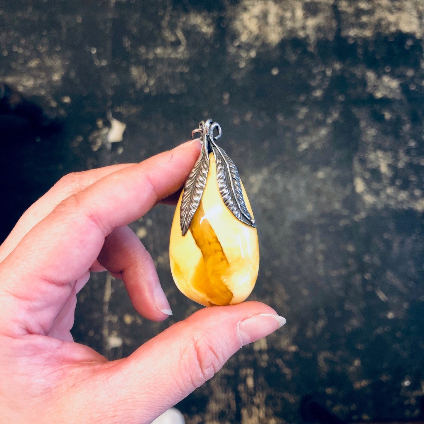 Vintage silver pendant with faceted butterscotch amber stone held in hand against dark background