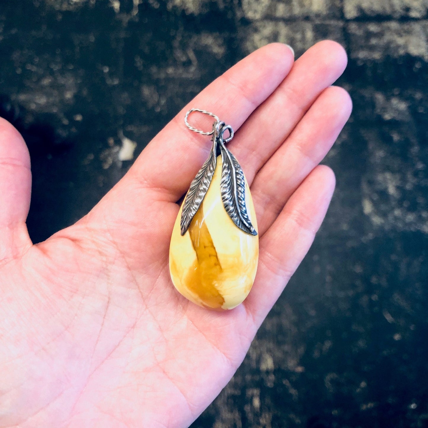 Vintage butterscotch amber pendant set in sterling silver, held in palm of hand against weathered wooden background