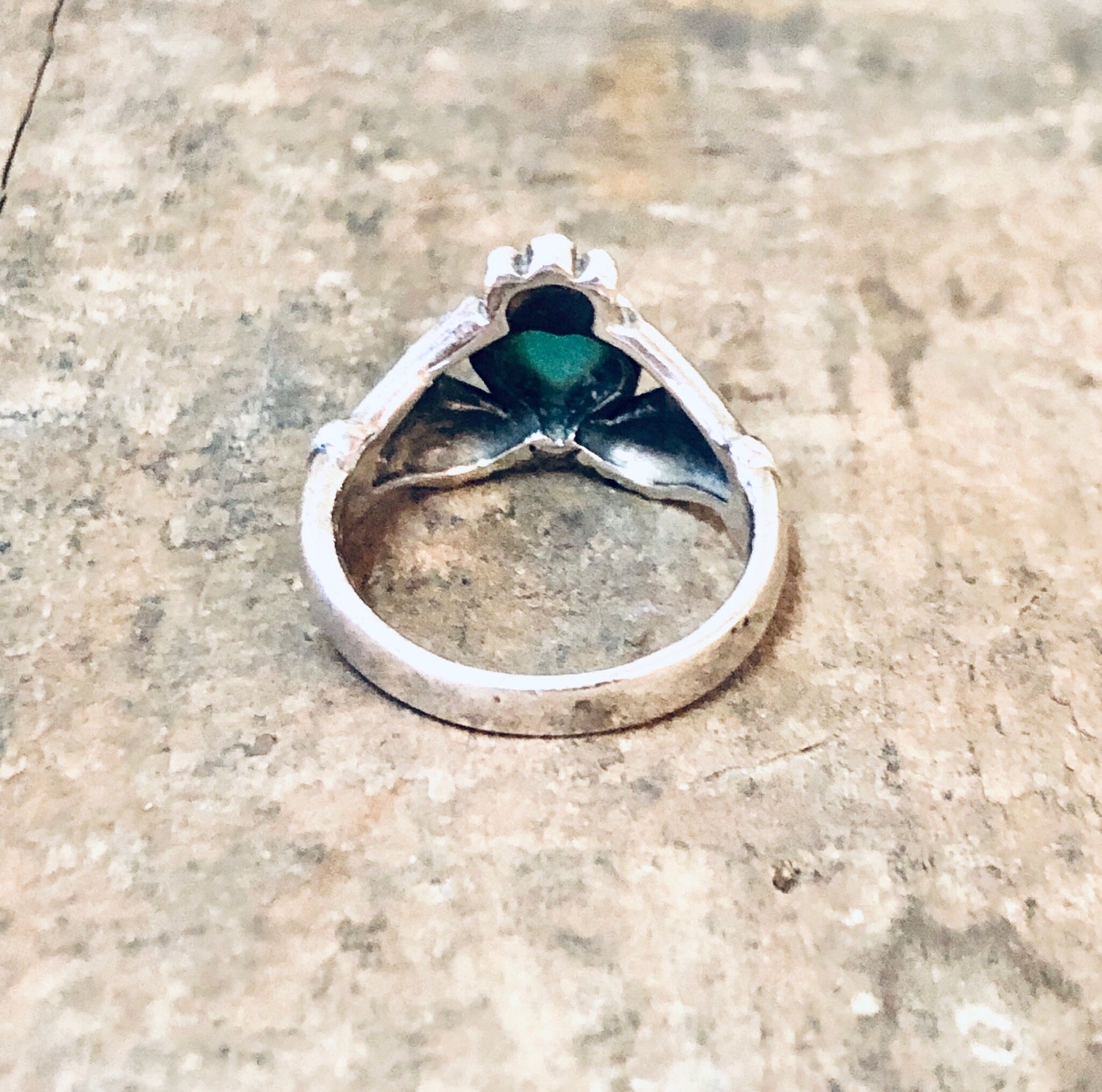 Vintage silver Claddagh ring with green enamel heart, representing love and loyalty, on rustic wooden surface.