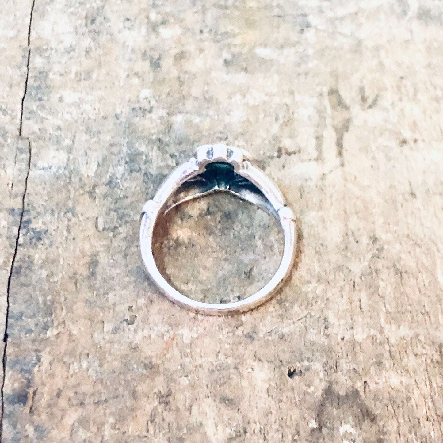 Vintage silver Claddagh ring with green enamel heart on weathered wooden surface