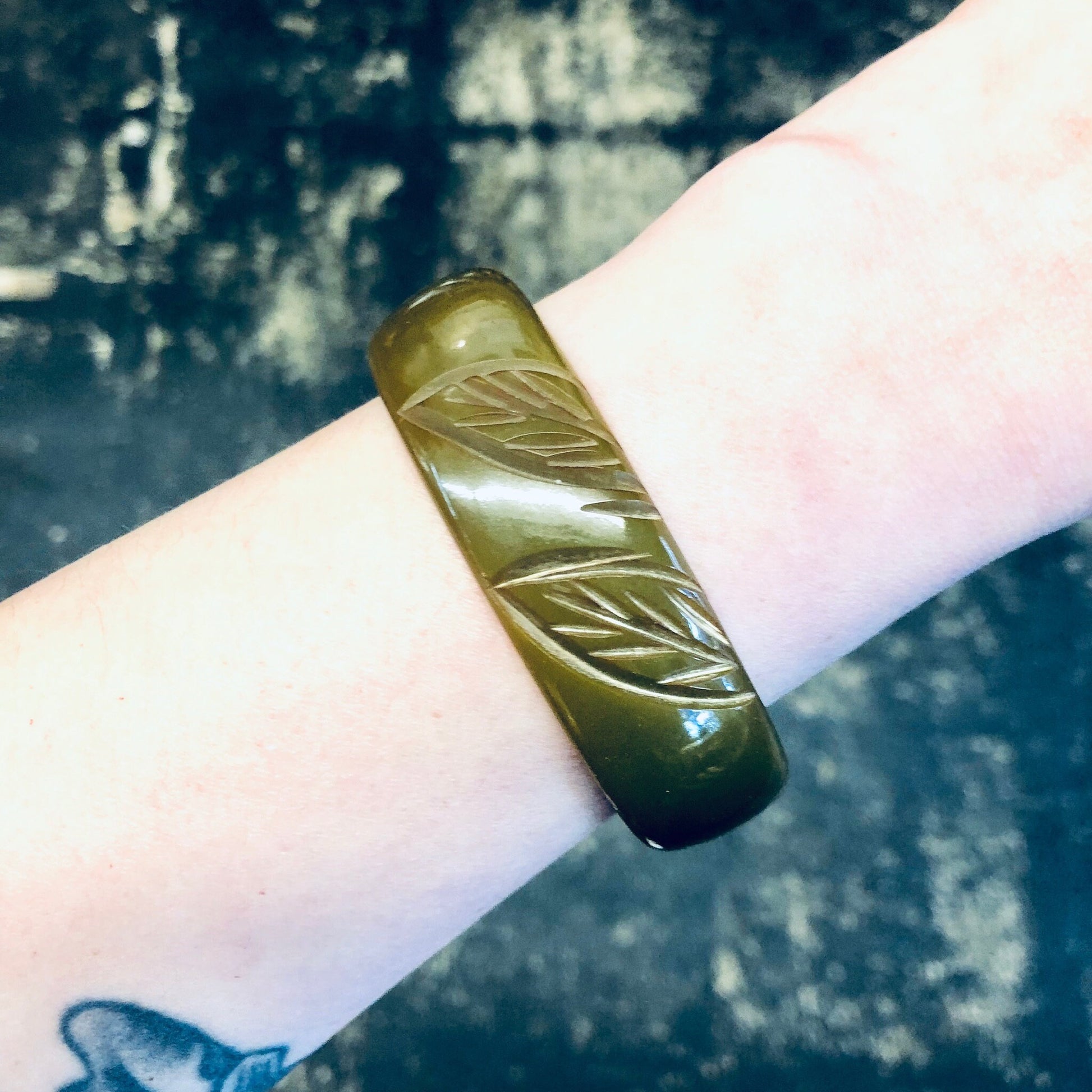 Vintage moss green Bakelite bangle bracelet with etched leaf design, shown on wrist against dark background