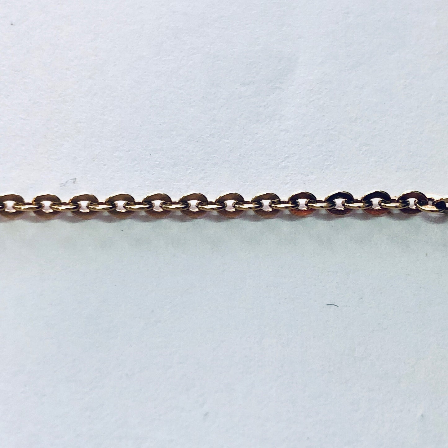 Gold chain with small, round links against a plain background