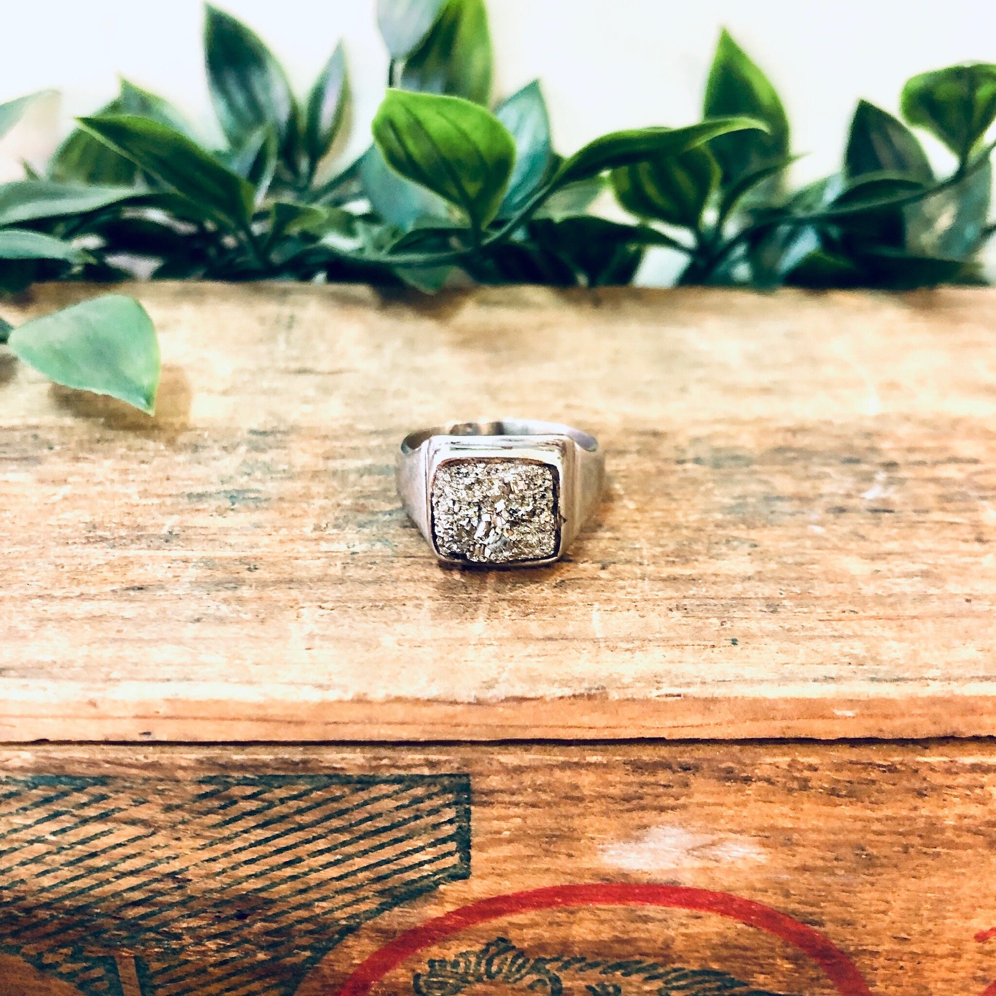 Vintage silver cocktail ring with raw quartz stone on rustic wooden surface with green leaves in background