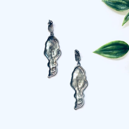 Vintage silver dangle earrings featuring art nouveau style lady figures, set against green leaves on a white background.