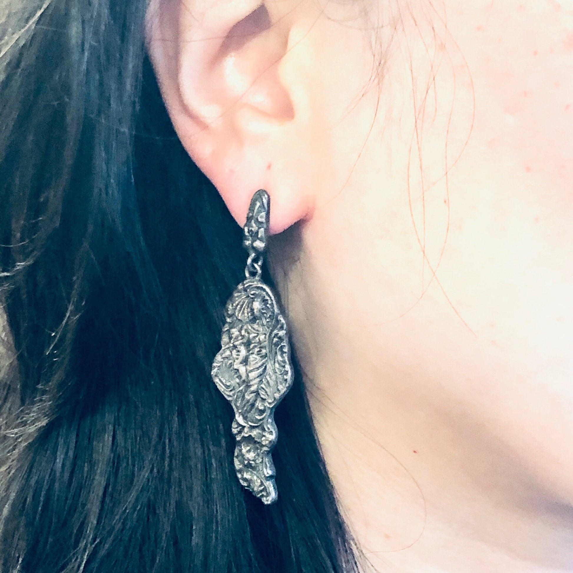 Vintage silver figural dangle earrings in Art Nouveau style depicting a lady's profile, worn on a woman's ear with dark hair.