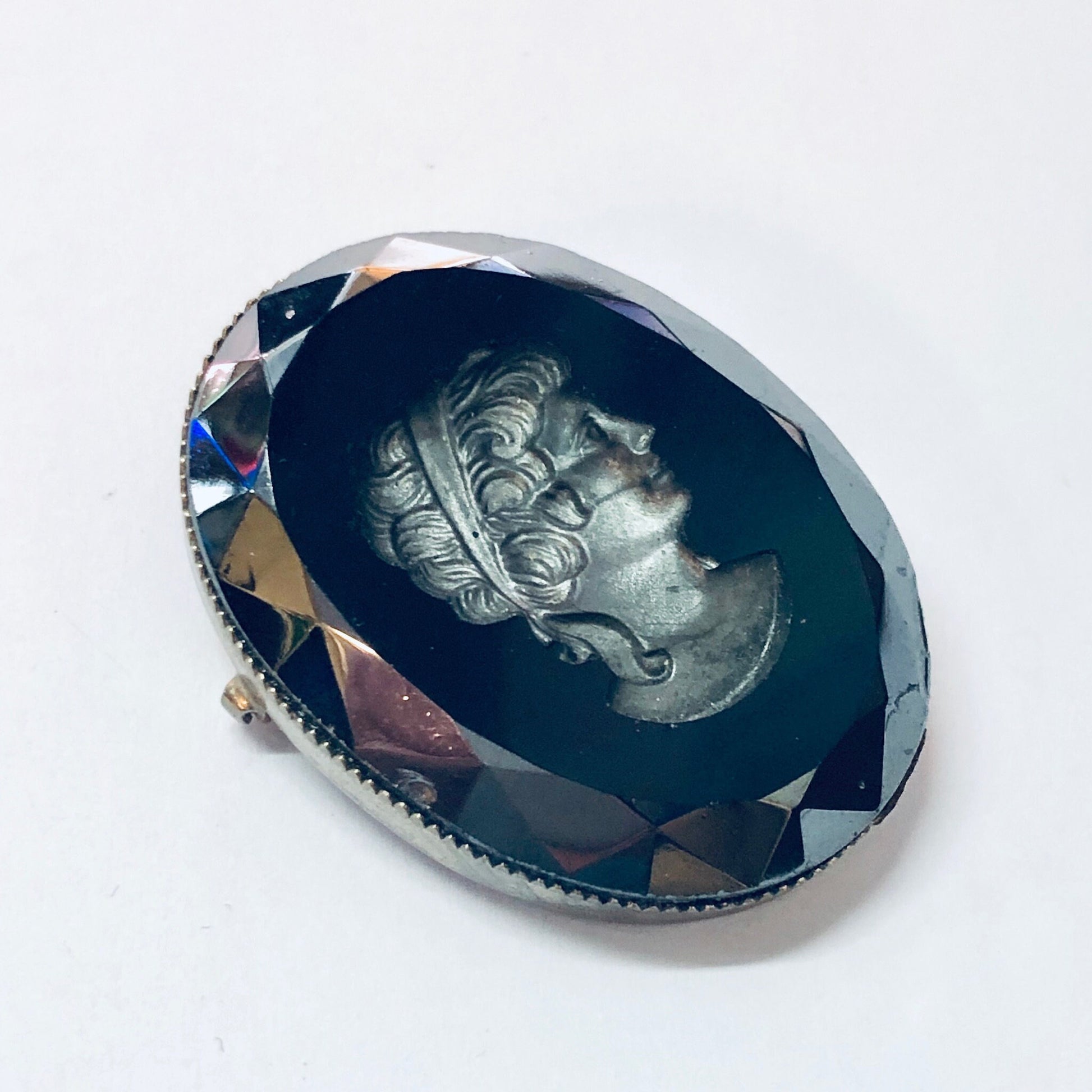 Vintage silver-toned cameo brooch featuring an etched black cameo with an intricate facial profile design, set against a multifaceted dark blue crystal background.