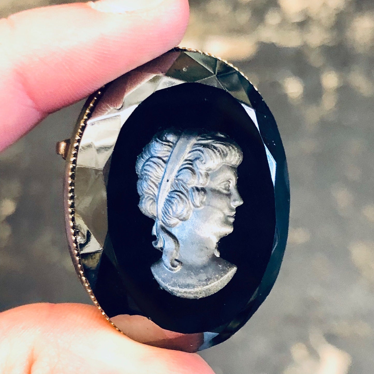 Vintage black cameo brooch with etched silver-toned profile portrait, held in hand against blurred background