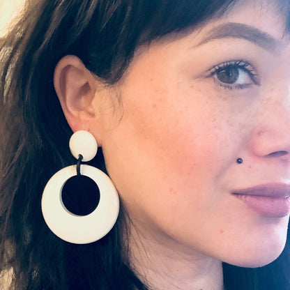 Close-up portrait of a woman wearing large vintage black and white circular dangle earrings, with blue eyes and dark hair pulled back.