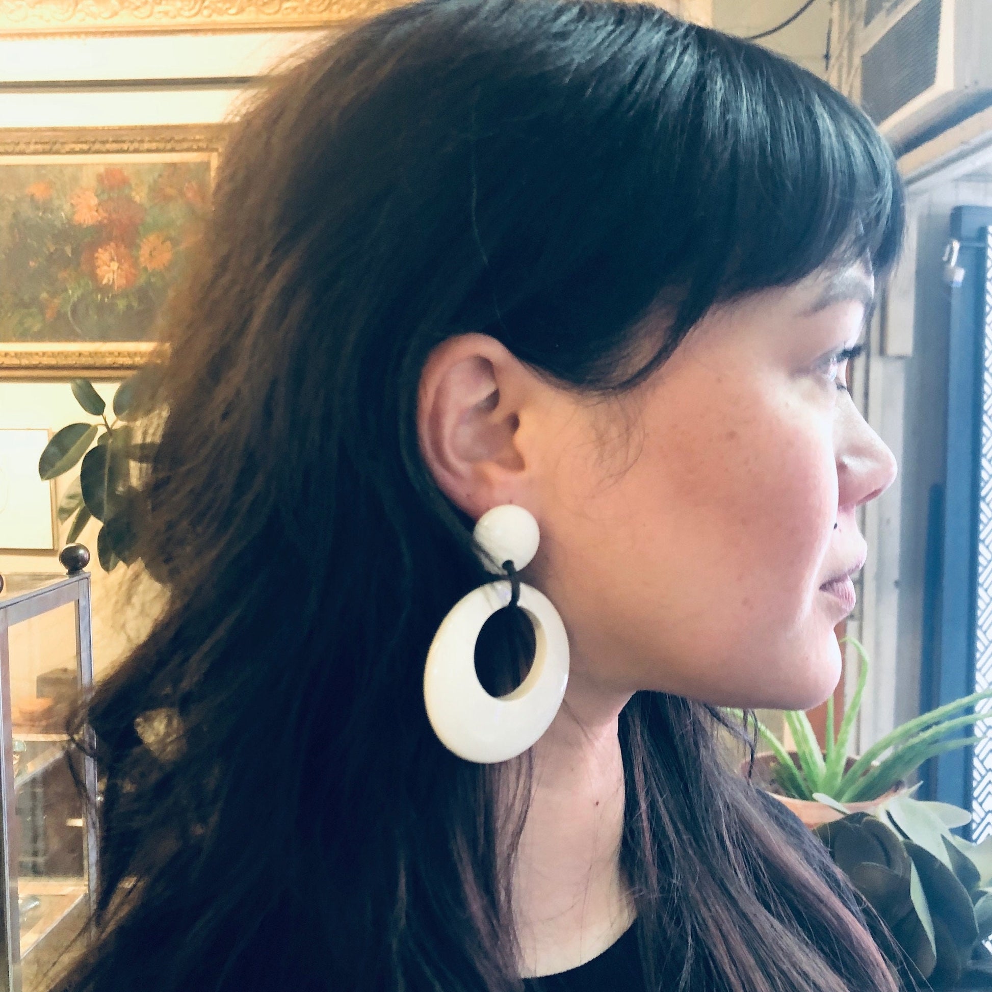 Side view of a woman with long dark hair wearing large white oval dangle earrings with black centers