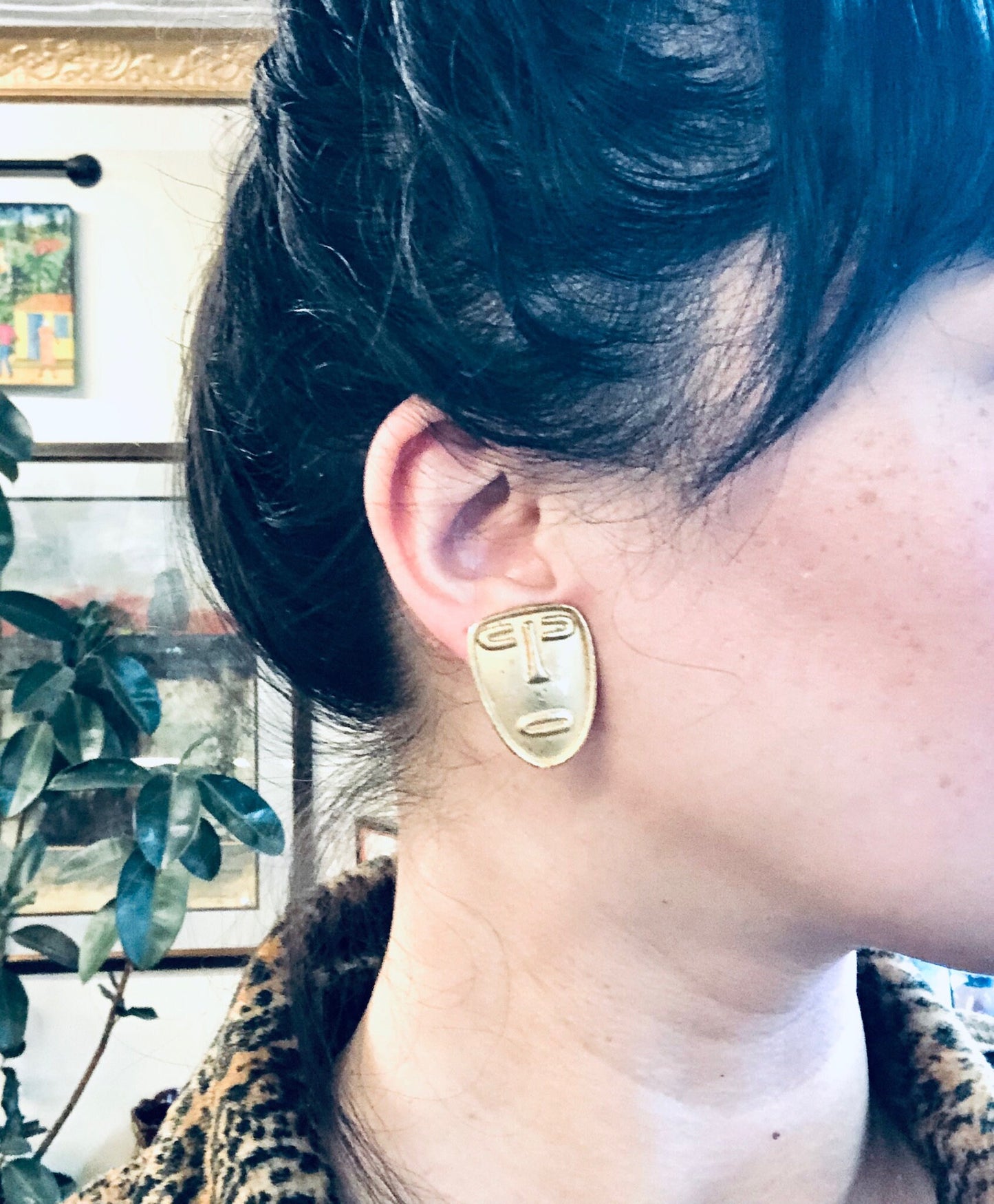 Vintage gold toned abstract face clip-on earrings, worn by a person with dark hair in a leopard print coat, providing a unique and stylish look for masks or as statement jewelry pieces.