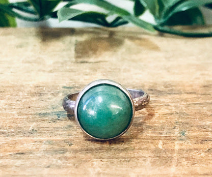 Vintage silver ring with round green cabochon gemstone on wooden surface with greenery in background