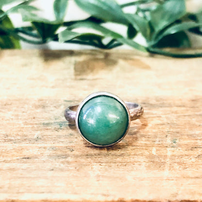 Vintage silver ring with round green cabochon gemstone on wooden surface with green leaves in background