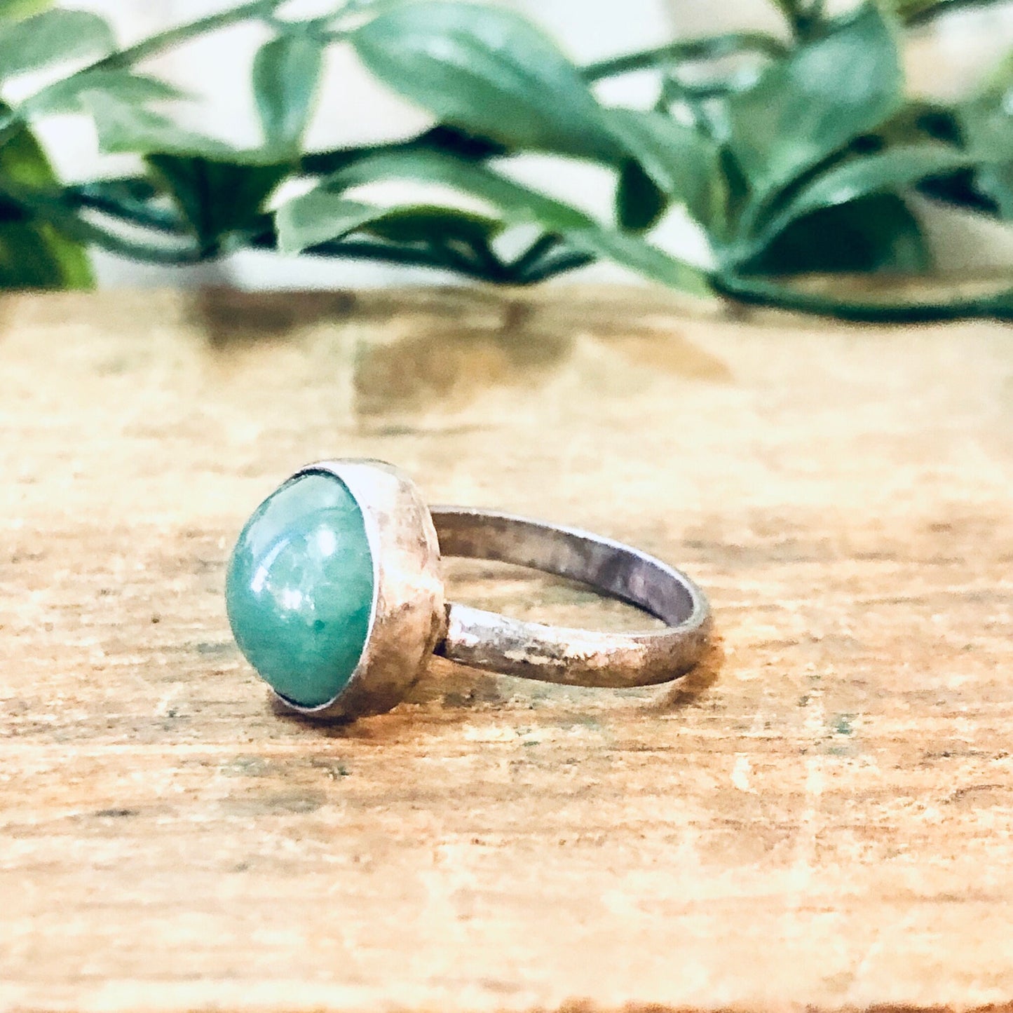 Vintage silver ring with round green gemstone cabochon on wooden surface with greenery in background