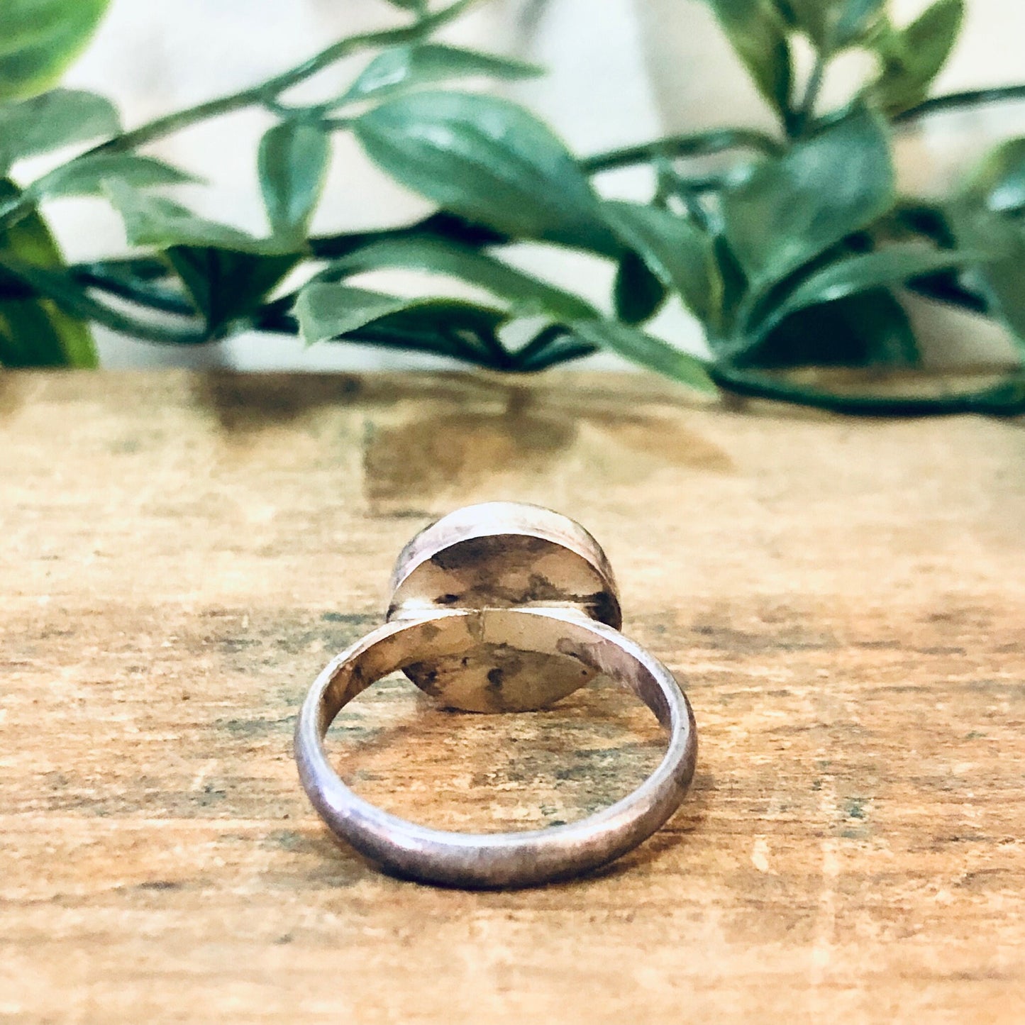 Vintage silver round cabochon ring with green gemstone on rustic wooden surface with greenery in background