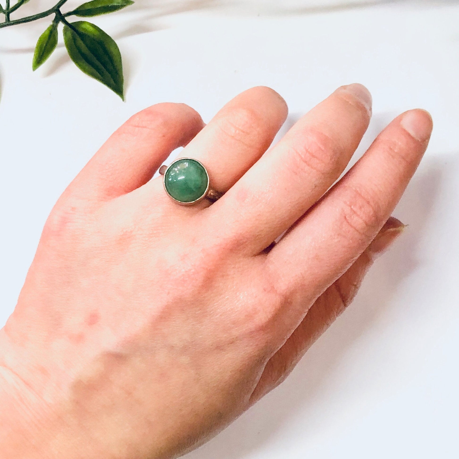 Vintage silver ring with round green cabochon gemstone on a hand with green leaves in the background