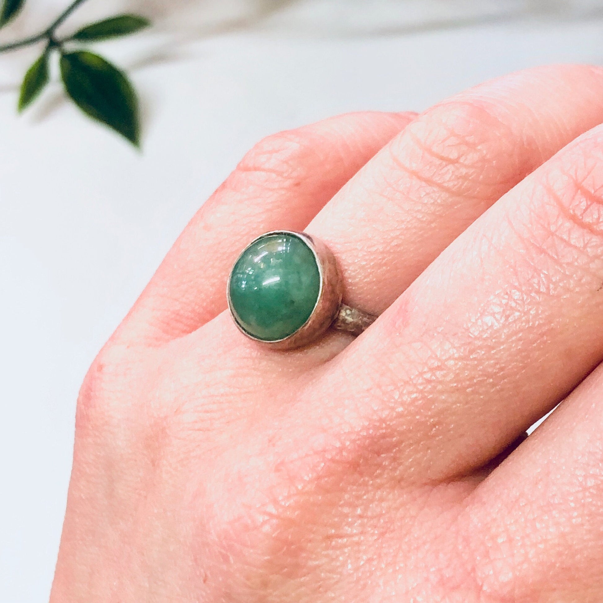 Vintage silver ring with round green gemstone cabochon on hand near leaves