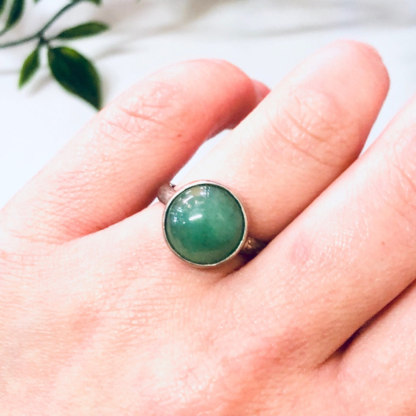 Vintage silver ring with round green gemstone cabochon on hand with leaves in background