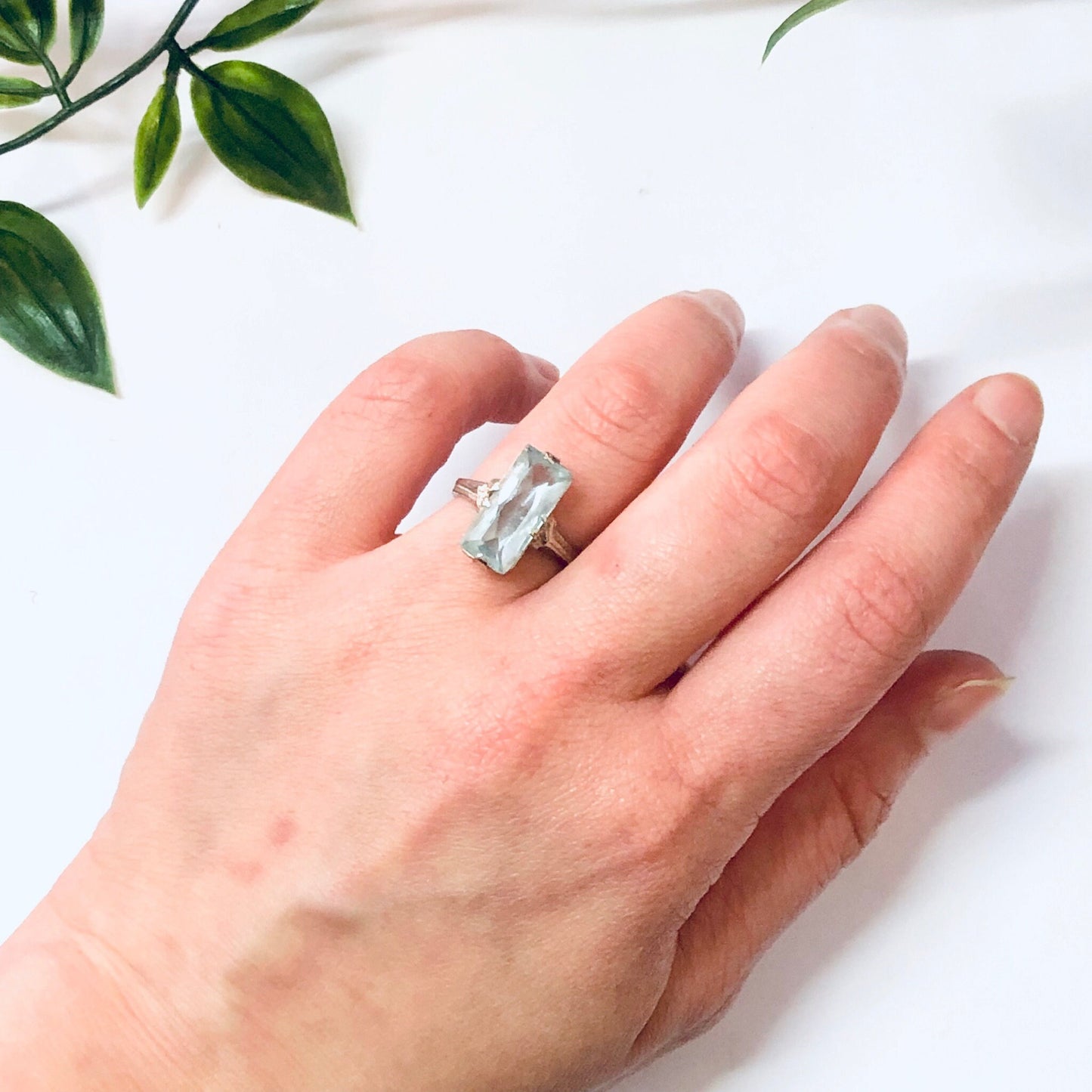 Vintage 18K white gold aquamarine ring on a hand with green leaves in the background