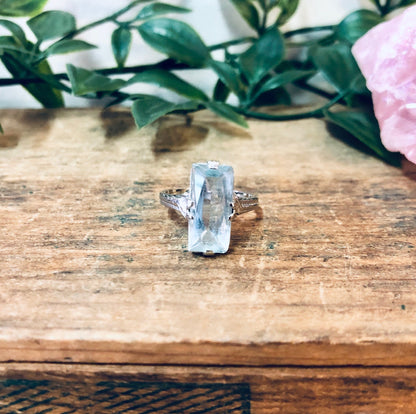 Vintage 18K white gold aquamarine ring on rustic wooden surface with pink flower and green leaves