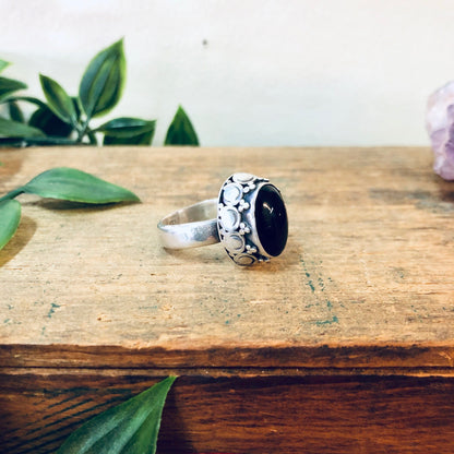 Vintage silver ring with large black onyx gemstone on wooden surface with leaves