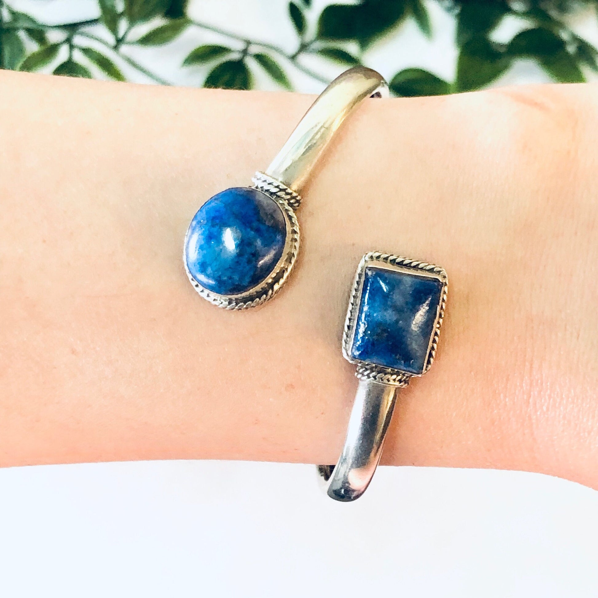 Vintage silver bangle bracelet with two round blue lapis lazuli stones set in spiral design against leaves background.