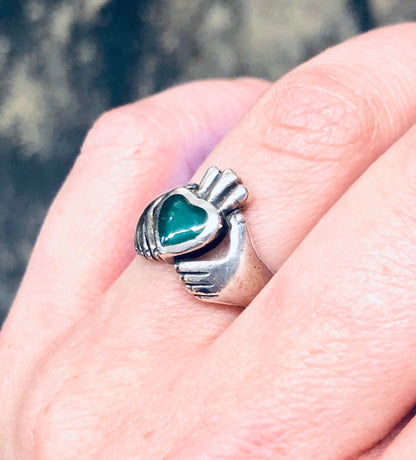 Vintage silver Claddagh ring with green enamel heart on finger, symbolizing love and loyalty