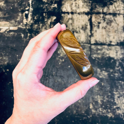 Hand holding a vintage brown bakelite bangle bracelet with leaf etching against a grungy concrete background.