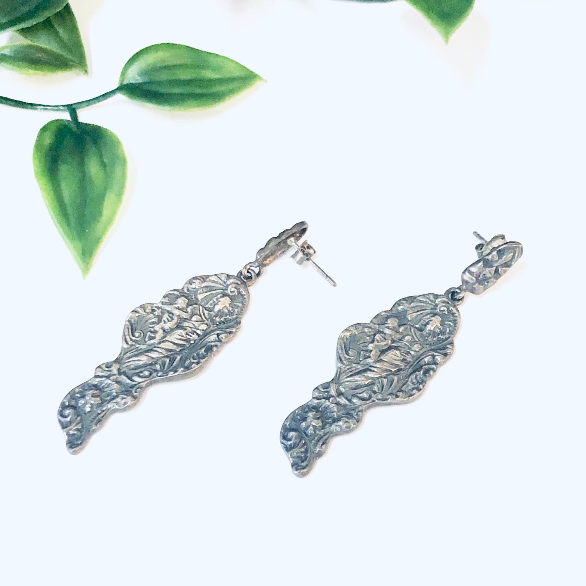 Vintage silver art nouveau style figural lady dangle earrings on white background with green leaves