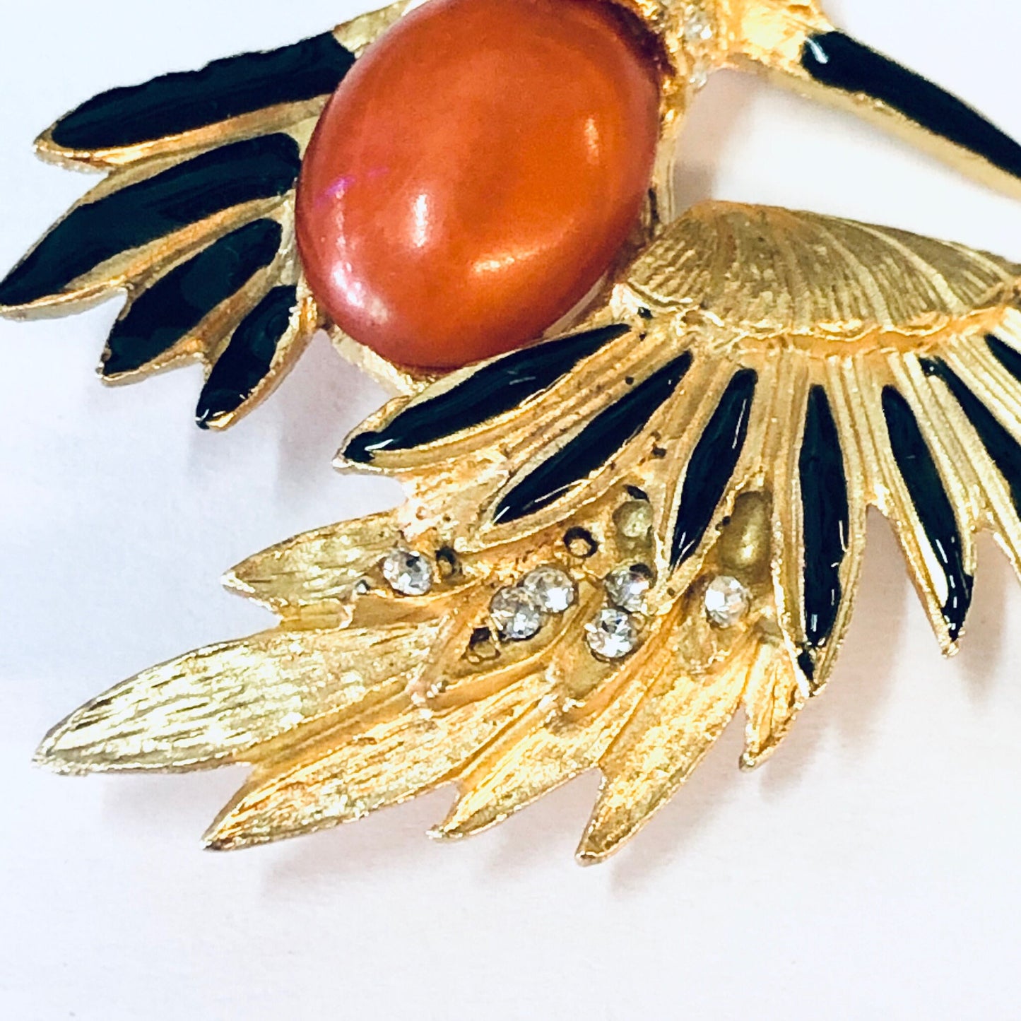 Vintage gold-toned bird brooch pin with orange stone, black enamel accents, and rhinestone details, showcasing intricate feather design in a striking jewelry piece from the past.