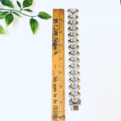 Vintage silver link bracelet with heart-shaped links, made in Italy, shown alongside a wooden ruler and green leaves.