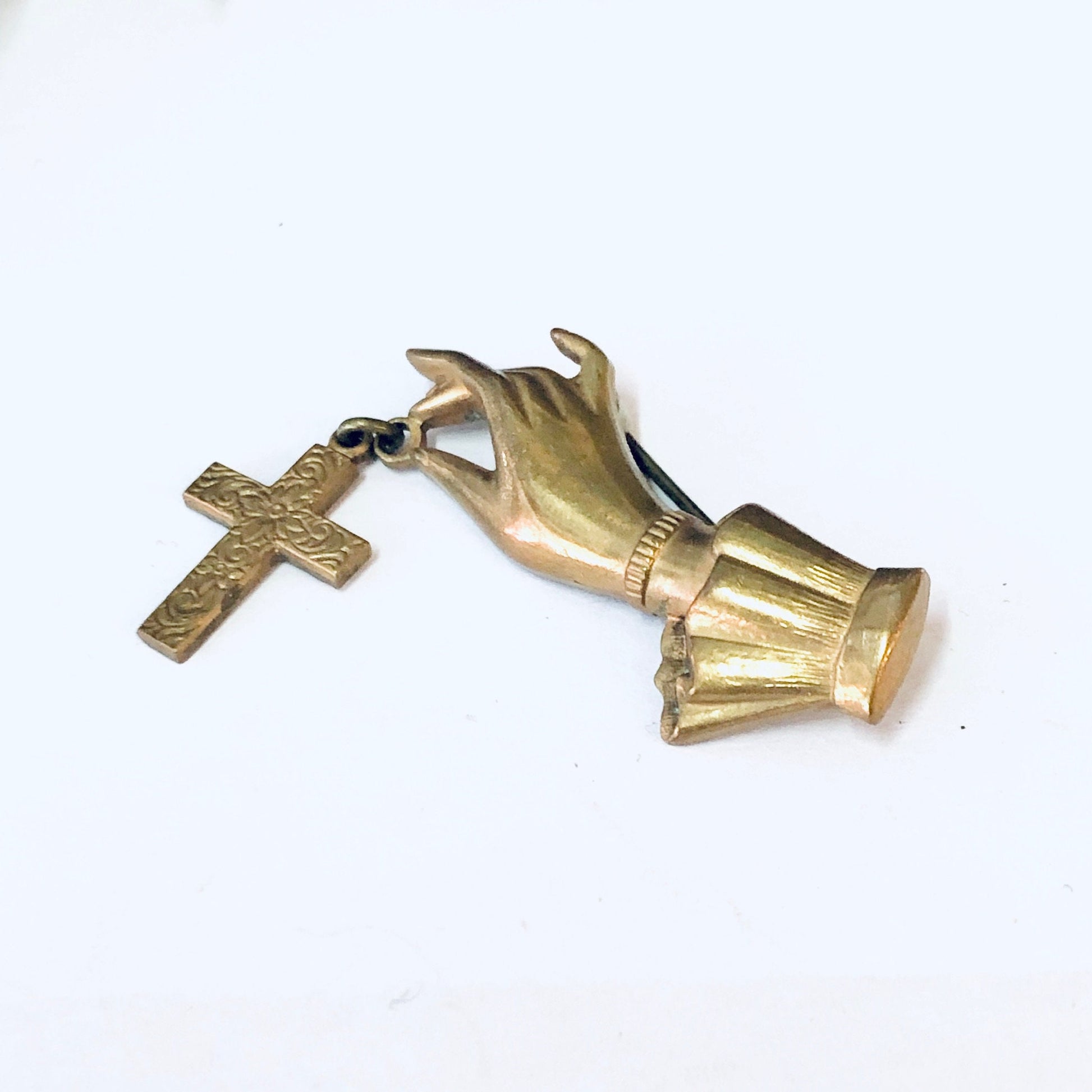 Vintage gold-toned brooch featuring hands holding a cross, religious costume jewelry pin.