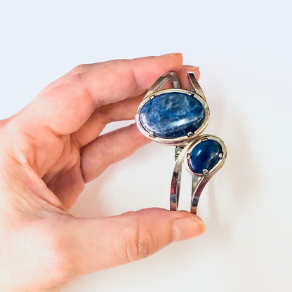 Vintage silver-toned cuff bracelet with blue stones held in a hand, showing the unique hinged wrap design of this eye-catching costume jewelry piece.