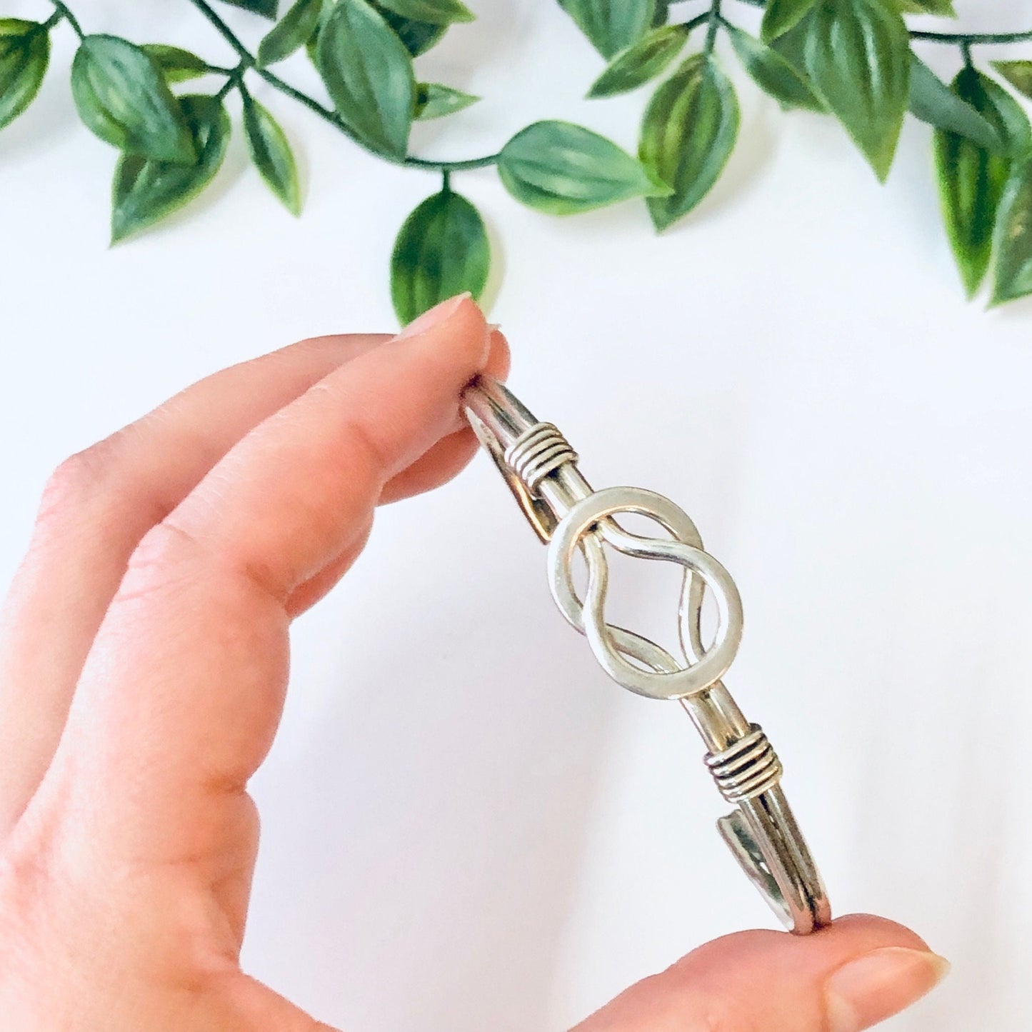 Vintage silver Celtic knot cuff bracelet held in hand with green foliage in background