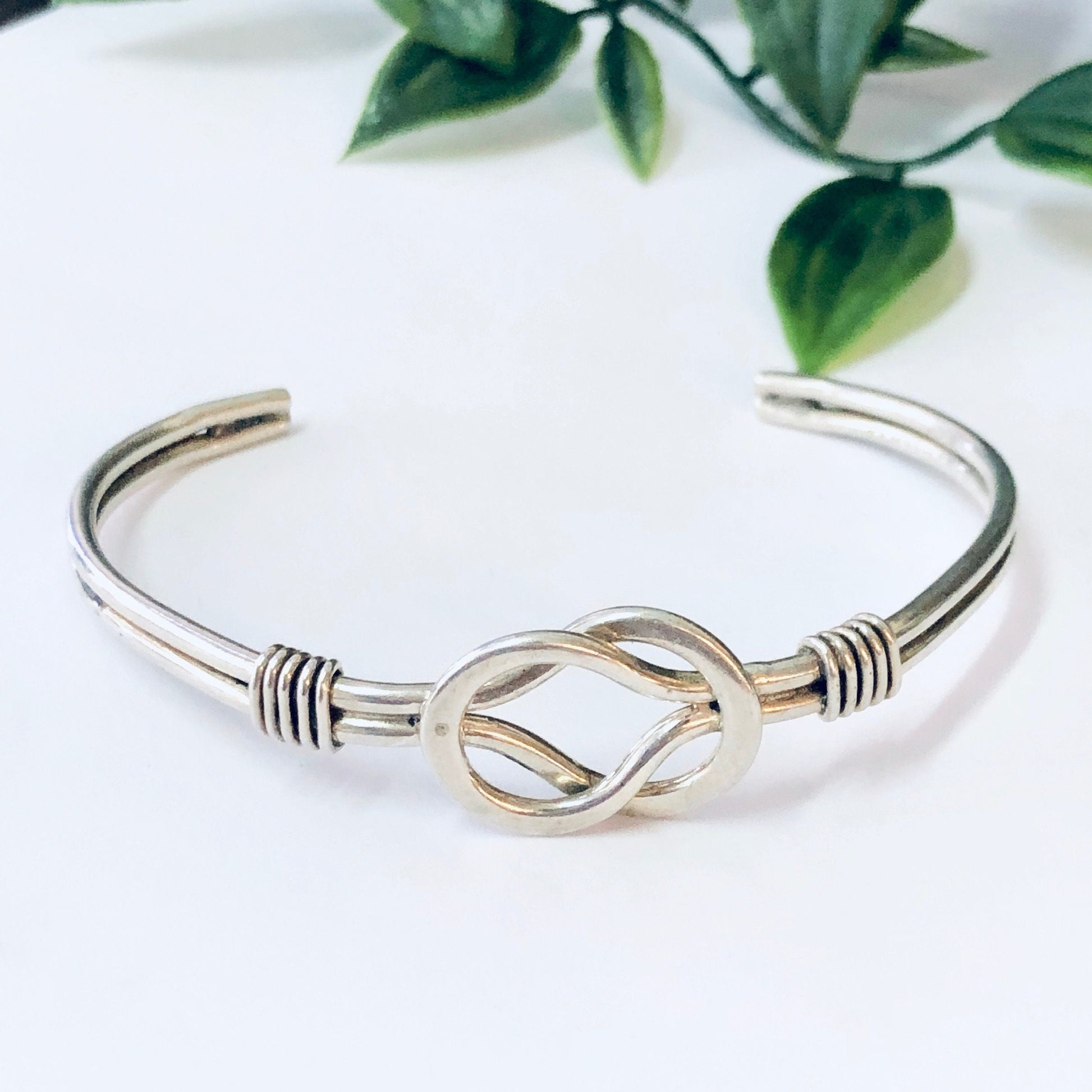 Vintage silver Celtic knot cuff bracelet with unique, simple design on white background with green leaves.