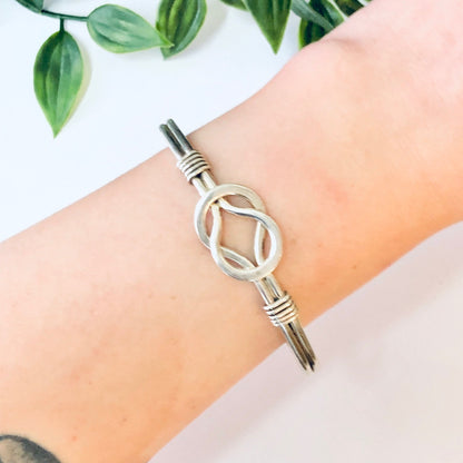 Silver knot cuff bracelet with Celtic design on wrist next to plant leaves