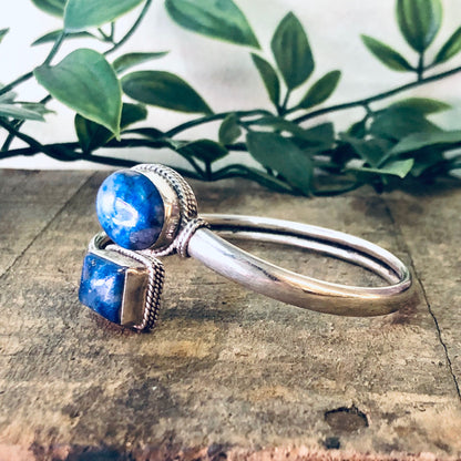 Vintage silver bangle bracelet with blue lapis lazuli gemstone, spiral cuff design, set against rustic wooden background with greenery.