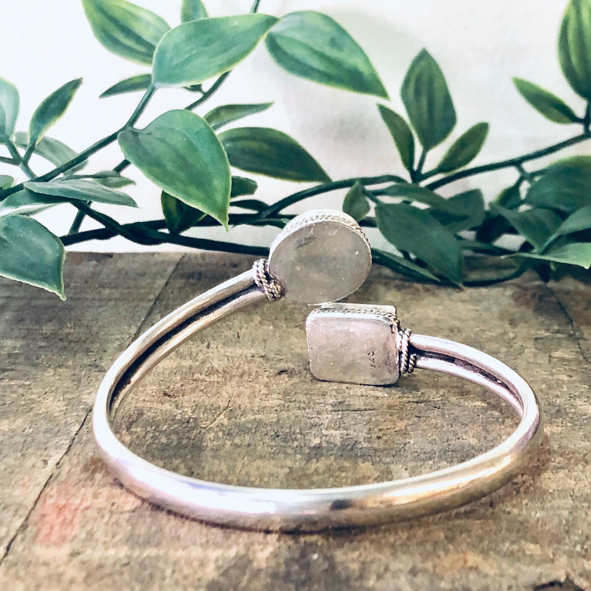 Vintage silver bangle bracelet with blue lapis stone, spiral design cuff, on rustic wooden surface with green leaves in background