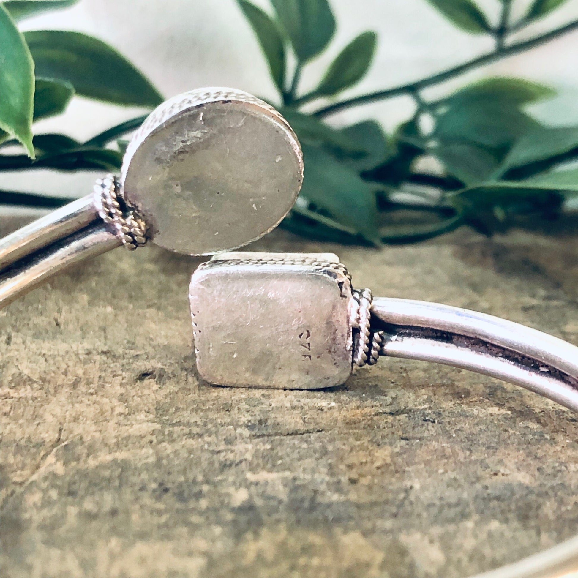 Vintage silver bangle bracelet with blue lapis lazuli gemstone accents, featuring a spiral twisted cuff design, displayed on a stone surface with green foliage in the background.