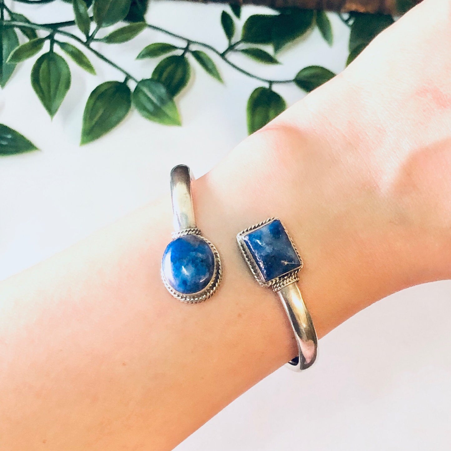 Vintage silver bangle bracelet with blue lapis stones on woman's wrist, with greenery in the background